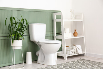 Fototapeta na wymiar Toilet bowl, houseplant and shelving unit with bathroom accessories near wall