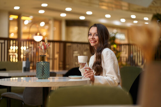 Young beautiful stylish woman in white blazer with cup od coffee sitting in restaurant