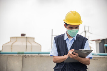 Male worker wearing a yellow helmet with a clipboard works in an industrial factory.