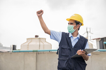 Male worker wearing a yellow helmet with a clipboard works in an industrial factory.