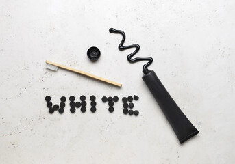 Opened tube with activated carbon toothpaste, toothbrush and word WHITE made of pills on light background