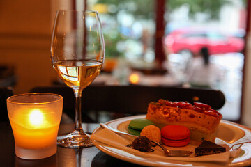 A burning candle, a glass of wine and dessert on the table.