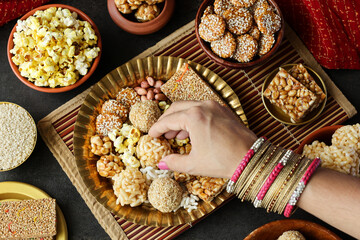 Til chikki peanut chikki Murmura ladoo laddu Revdi popcorn woman hand serving winter food Indian...
