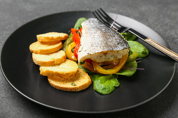 Plate of tasty sea bass fish with vegetables on black background