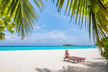 The girl is sitting on a beach lounger on a paradise island with azure water and exotic vegetation