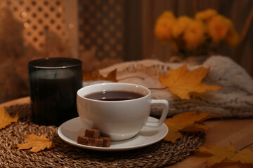 Cup of aromatic tea with sugar and autumn leaves on wooden table indoors
