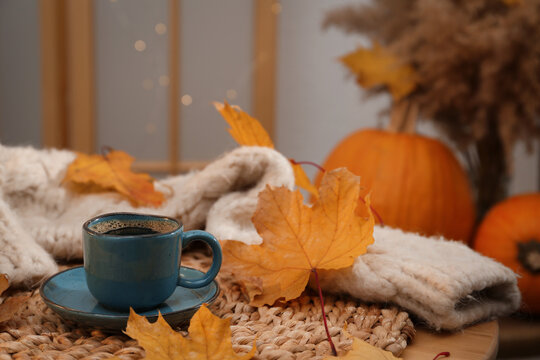 Cup of aromatic coffee, sweater and autumn leaves on table indoors, space for text