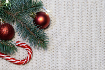 New Year's, xmas attributes on a white knitted background with a fir branch, red Christmas balls and candy. Background with empty place for text. New Year, Christmas card. Christmas background