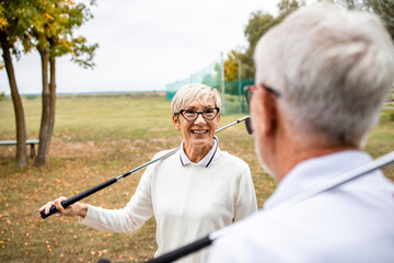 An active senior couple with golf clubs enjoying free time outdoors.