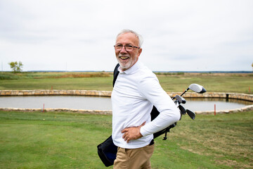 Portrait of wealthy senior golfer with golf clubs enjoying free time outdoors.