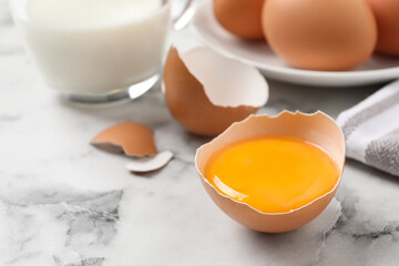 Cracked eggshell with raw yolk on white marble table, closeup. Space for text