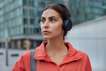 Photo of serious brunette sportswoman listens music in wireless headphones enjoys audio track...