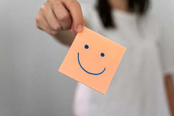 Hand holding orange happy smile face paper cut, mental health assessment, child positive wellness,...