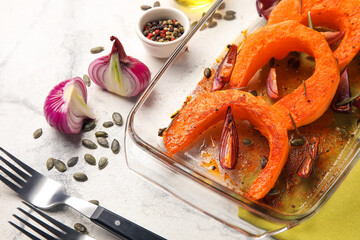 Dish with tasty baked pumpkin pieces on white marble background, closeup