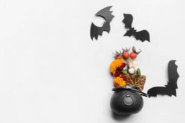 Witch's cauldron with flowers and paper bats on white background