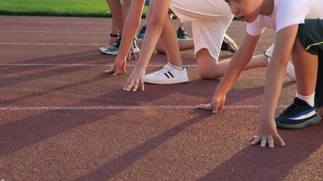 A group of boys kids runners lined up ready to race on the treadmill at the stadium on a bright sunny day. The coach prepares athletes for competitions. Boys in colorful uniforms at the stadium.