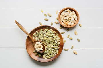 Plate and bowl with pumpkin seeds on white wooden background