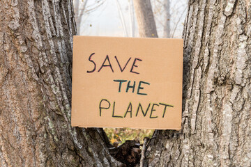 Cardboard sign placed on the trunk of a tree with the slogan -Save the Planet-