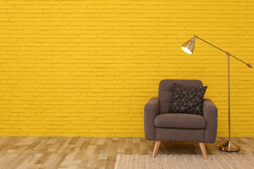 Stylish armchair and lamp near yellow brick wall in room, space for text. Interior design