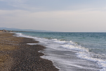 Strand and Mittelmeer, mit Wellen und Horizont bei leicht bedecktem Himmel