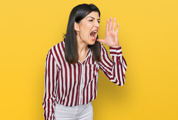 Beautiful brunette woman wearing striped shirt shouting and screaming loud to side with hand on mouth. communication concept.