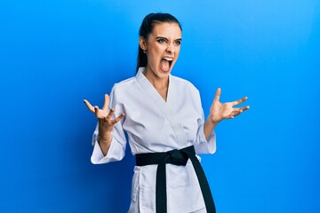 Beautiful brunette young woman wearing karate fighter uniform with black belt crazy and mad...