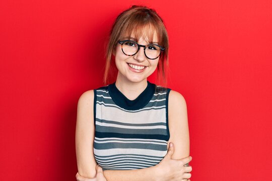 Redhead young woman wearing casual clothes and glasses happy face smiling with crossed arms looking at the camera. positive person.
