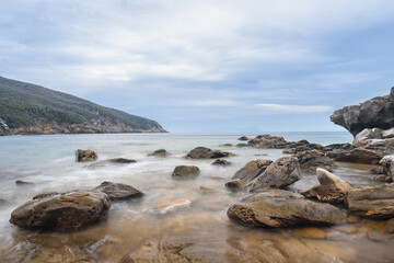 Felsen in der Bucca delle Fate mit Blick Richtung Isola del Elba, Toskana, Italien mit Wolken und Bergen