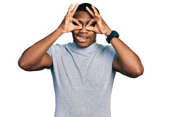 Young black man wearing casual t shirt doing ok gesture like binoculars sticking tongue out, eyes looking through fingers. crazy expression.