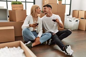 Young caucasian couple toasting with red wine glass sitting at new home.