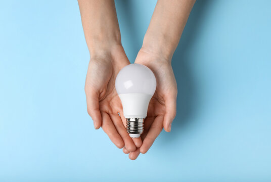 Woman holding light bulb on color background, top view