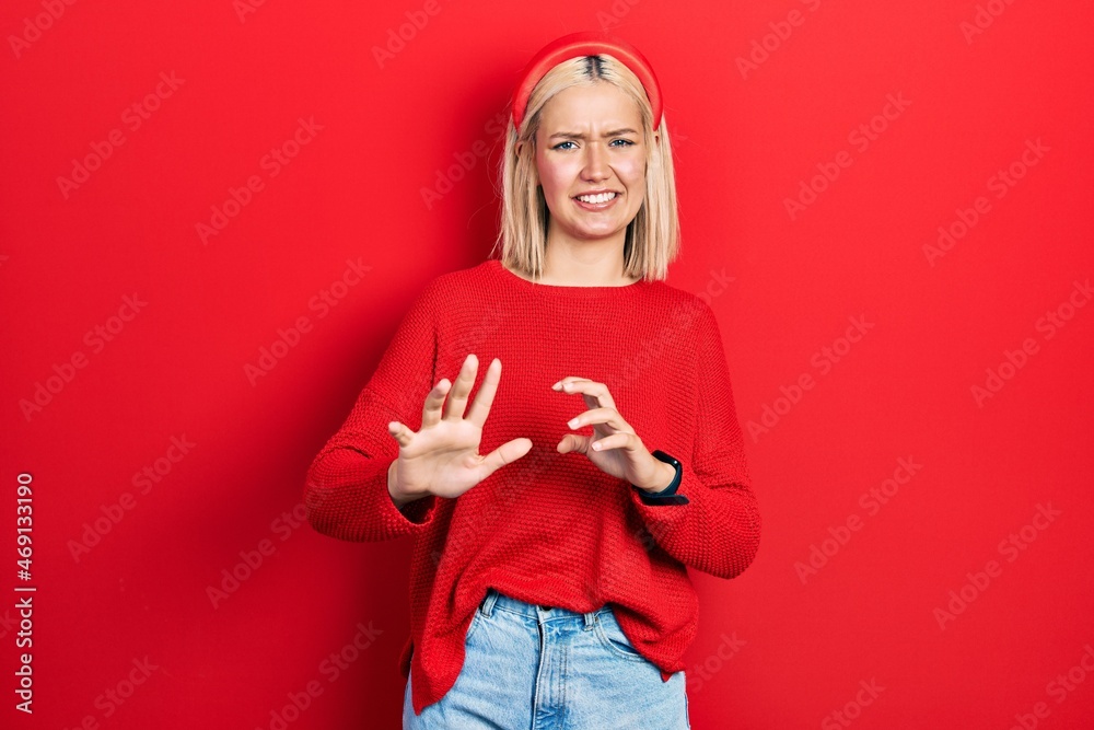 Sticker Beautiful blonde woman wearing casual red sweater disgusted expression, displeased and fearful doing disgust face because aversion reaction. with hands raised