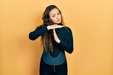 Young hispanic girl wearing diver neoprene uniform doing time out gesture with hands, frustrated...