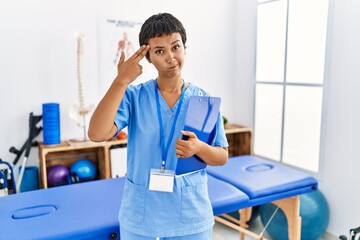 Obraz premium Young hispanic woman with short hair working at pain recovery clinic shooting and killing oneself pointing hand and fingers to head like gun, suicide gesture.