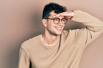 Young hispanic man wearing casual clothes and glasses very happy and smiling looking far away with hand over head. searching concept.