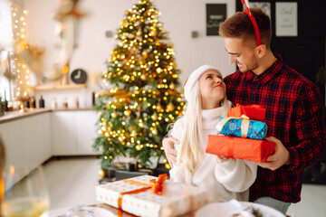 Cheerful young male and female Exchange of Christmas gifts. Young couple opening gift box near Christmas tree. Romantic day. Winter holidays.
