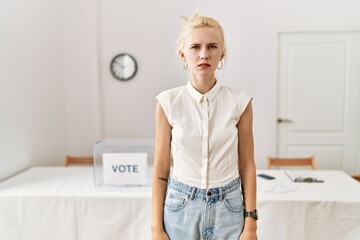 Beautiful caucasian woman standing by voting ballot at election room with serious expression on...