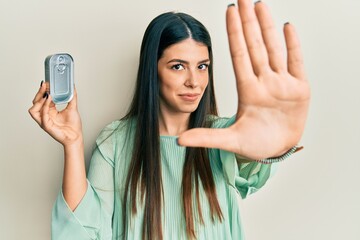 Young hispanic woman holding canned food with open hand doing stop sign with serious and confident expression, defense gesture