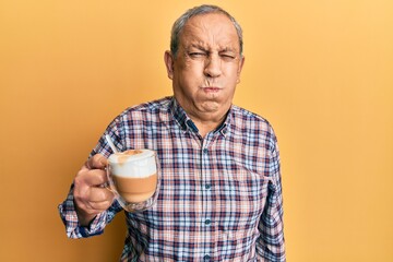 Handsome senior man with grey hair drinking a cup coffee puffing cheeks with funny face. mouth inflated with air, crazy expression.