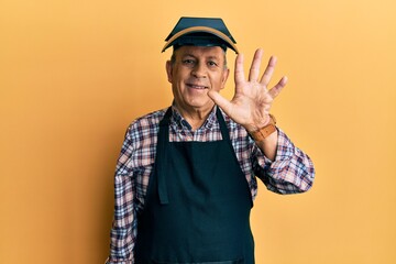 Handsome senior man with grey hair wearing welding protection mask showing and pointing up with fingers number five while smiling confident and happy.