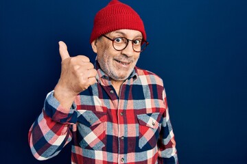 Naklejka premium Handsome mature man wearing hipster look with wool cap doing happy thumbs up gesture with hand. approving expression looking at the camera showing success.