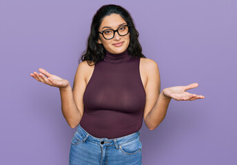 Brunette young woman wearing casual clothes and glasses clueless and confused expression with arms...