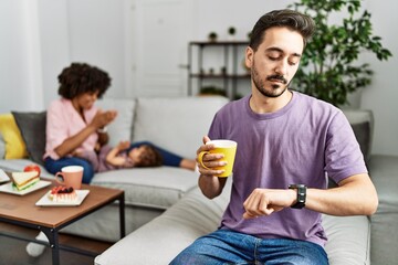 Hispanic father of interracial family drinking a cup coffee checking the time on wrist watch, relaxed and confident