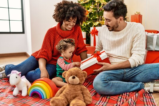 Couple and daughter holding gift sitting by christmas tree at home