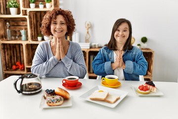 Family of mother and down syndrome daughter sitting at home eating breakfast praying with hands together asking for forgiveness smiling confident.