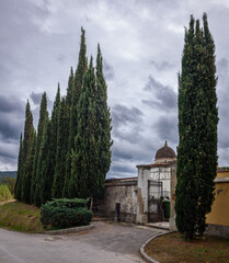 Fototapeta premium Friedhof mit Zypressen im Vordergrund, vor Wolken und mit toskanischen Hügeln im Hintergrund