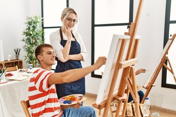 Art woman teacher smiling happy looking draw of paint student at studio.