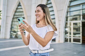 Young hispanic woman smiling confident using smartphone at street