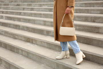 Stylish woman with trendy beige bag on stairs outdoors, closeup