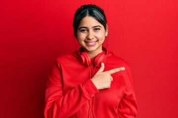 Young latin woman listening to music using headphones smiling cheerful pointing with hand and finger up to the side